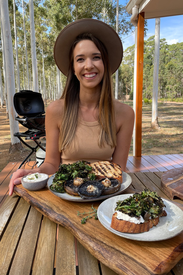 Laura Romeo smiling at a wooden table with grilled mushrooms and bruschetta